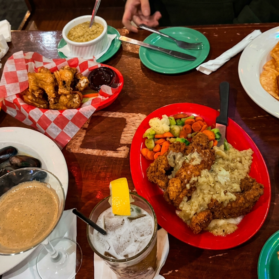 Restaurant table covered with fried seafood, mussels, chips, nachos, vegetables, dipping sauces, drinks, and creamy soup.